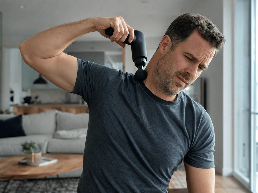 Man holding a massage gun against his upper back with one arm raised